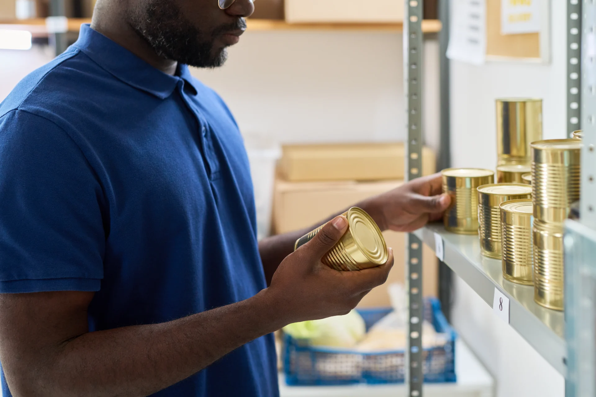 Young Adult Black Man Organizing Canned Goods on Shelf in Storage Room